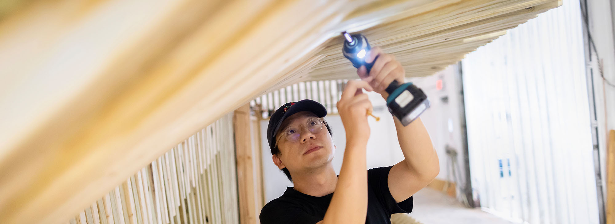 image of a young man using a drill to construct the inside of a cooling structure of wood